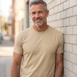 Basic T-shirt, Kit - 2000 | Livsstilsfoto af en veltrænet mand omkring 55 år med kortklippet gråt/salt-og-peber hår og skægstubbe, iført en almindelig hvid rundhalset T-shirt uden tryk.