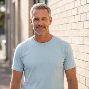 Basic T-shirt, Lys Blå - 2000 | Livsstilsfoto af en veltrænet mand omkring 55 år med kortklippet gråt/salt-og-peber hår og skægstubbe, iført en almindelig hvid rundhalset T-shirt uden tryk.