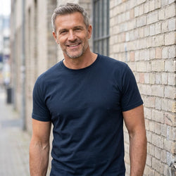 Basic T-shirt, Navy - 2000 | Livsstilsfoto af en veltrænet mand omkring 55 år med kortklippet gråt/salt-og-peber hår og skægstubbe, iført en almindelig hvid rundhalset T-shirt uden tryk.